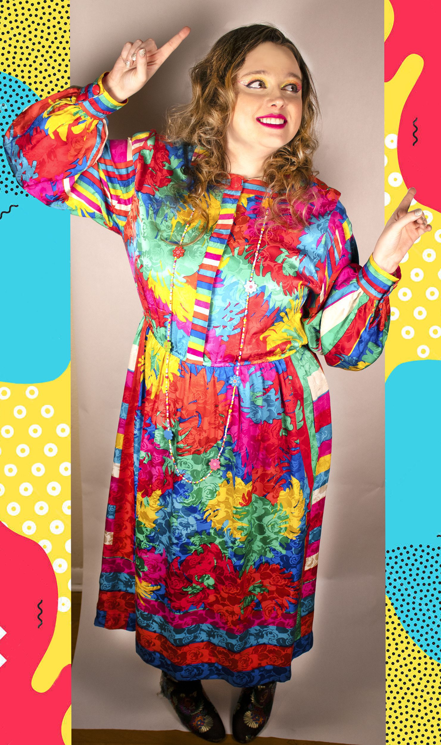 Right facing full body photo of Artist Chelsea Smith smiling while looking and pointing with both hands to the right. Chelsea is wearing a brightly colored dress and makeup along with a bright 80s inspired design background